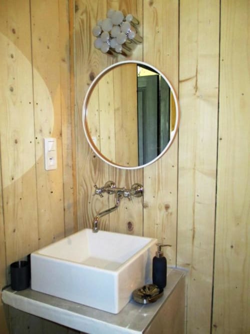 Lavabo moderne blanc rectangulaire avec miroir rond et panneaux muraux en bois à l'appartement Le Mas du Fort