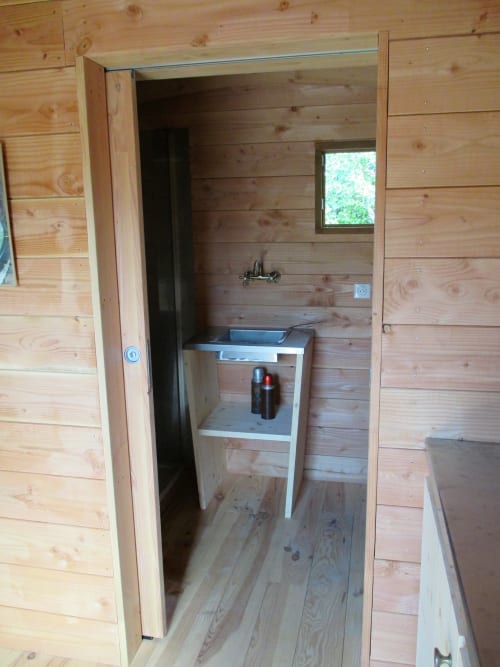 Intérieur en bois du gîte Le Mas du Fort à Gargas avec kitchenette équipée, évier et petite fenêtre donnant sur la zone piscine