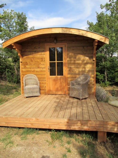 Cottage en bois avec toit cintrée au Mas du Fort à Gargas, terrasse, chaises en osier et porte vitrée