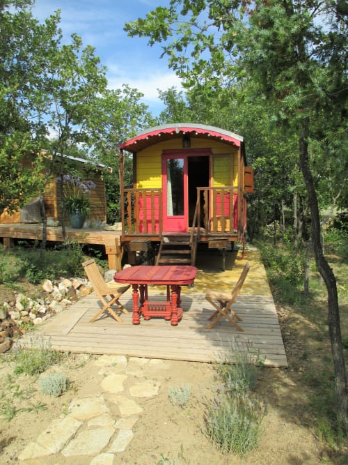 Caravane vintage colorée aux accents rouges au Mas du Fort, Gargas, entourée d'arbres avec terrasse en bois et mobilier extérieur