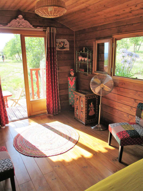 Intérieur de chalet en bois au Mas du Fort avec parquets, rideaux rouges, mobilier décoratif, ventilateur et vue sur la terrasse