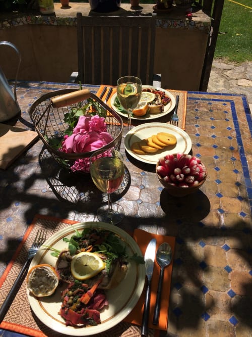 Repas en plein air au gîte Le Mas du Fort à Gargas avec assiettes dressées, vin, fleurs fraîches et panier de pain