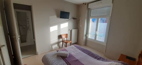 Chambre lumineuse à la Résidence Soansa du Gerardmer avec lit, TV, chaise en bois et fenêtres avec vue sur la ville à Soultzeren