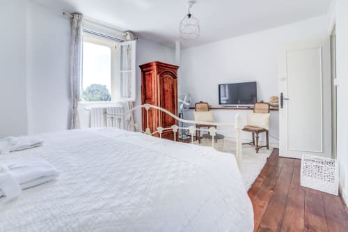 Chambre lumineuse du Manoir Le Coutureau avec lits blancs, armoire en bois, TV et vue sur le jardin
