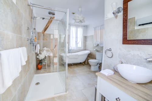 Salle de bain lumineuse au Manoir Le Coutureau avec douche vitrée, baignoire îlot, double vasque et accents en marbre