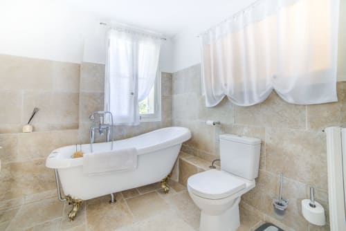 Salle de bains élégante du Manoir Le Coutureau avec baignoire sur pieds, toilettes et murs en carrelage beige baignés de lumière naturelle