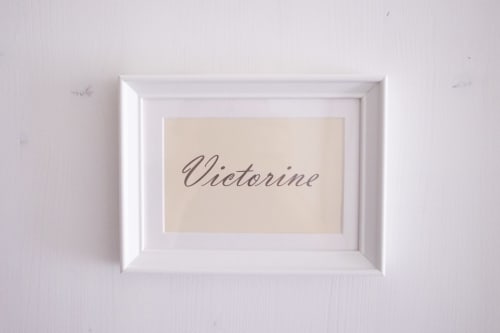 Plaque nominative blanche encadrée indiquant « Victorine » affichée sur mur blanc au gîte Manoir Le Coutureau