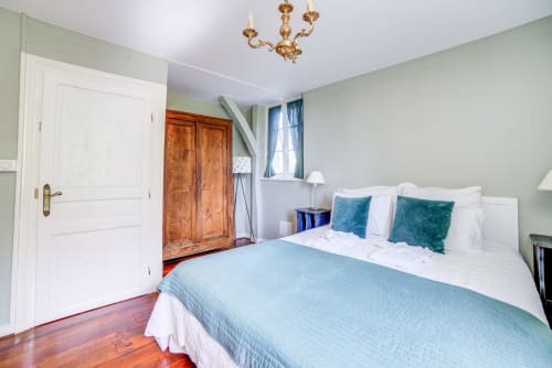 Chambre lumineuse au Manoir Le Coutureau avec murs vert pâle, literie blanche, coussins bleu-vert, armoire en bois et dorures