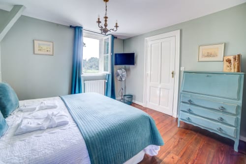 Chambre lumineuse du Manoir Le Coutureau avec décor bleu, vue sur le jardin, TV et commode turquoise sur parquet