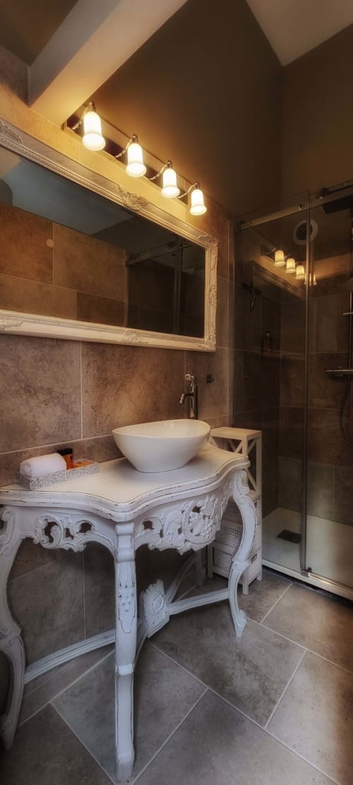 Salle de bains élégante au Manoir Le Coutureau avec vanité blanche ornementée, lavabo rond blanc, miroir encadré et douche à l'italienne