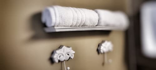 Serviettes blanches roulées sur étagère avec crochets décoratifs fleur-de-lis dans la salle de bain de la chambre du Manoir Le Coutureau