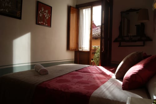 Chambre lumineuse à Casa Peregrinando à Navarrete avec literie bordeaux et portes en bois ouvrant sur balcon avec vue sur la ville