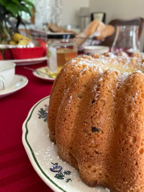Powdered kouglof cake on decorative plate at Le Clos d'Azel breakfast table with fresh bread and red linens