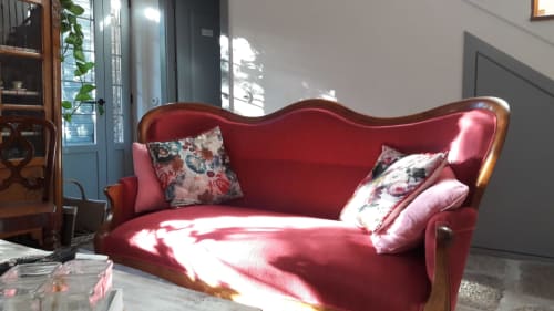 Élégant canapé rouge velours avec coussins floraux dans le salon de la Casa Rural La Perla, baigné de lumière naturelle