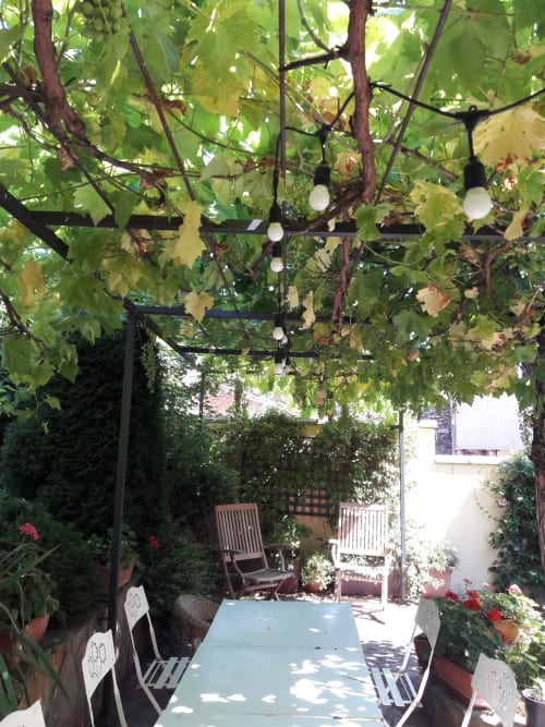 Casa Rural La Perla courtyard with vine-covered pergola, white chairs, and potted flowers in Hiendelaencina