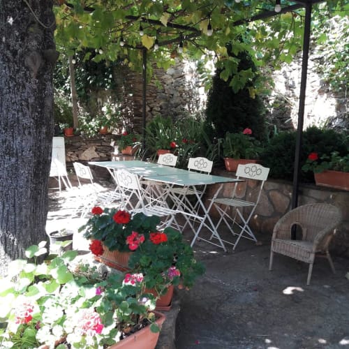 Charming outdoor patio at Casa Rural La Perla with white folding chairs, dining table, and vibrant red geraniums in