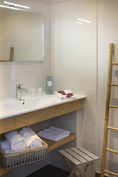 Salle de bain moderne à La Maison De Siloe avec carrelage blanc métro, vanité en bois, échelle à serviettes en bambou et rangements organisés