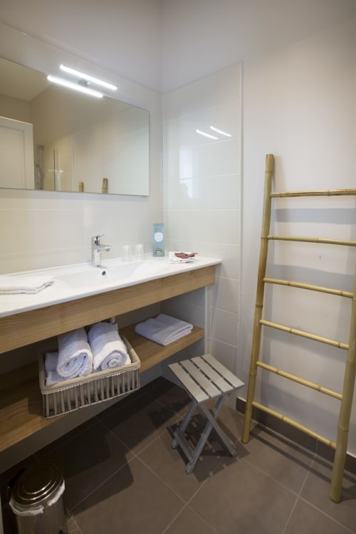 Salle de bain moderne à La Maison De Siloe avec meuble-lavabo en bois, carrelage blanc, miroir et porte-serviettes en bambou à Villefranche de