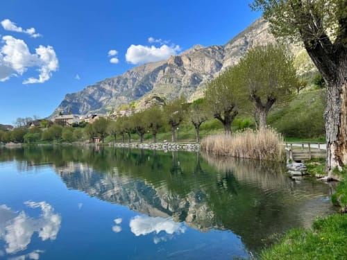 Vue paisible au bord du lac de l'Hôtel Marjori au Lauzet-Ubaye avec chaîne de montagnes et arbres centenaires