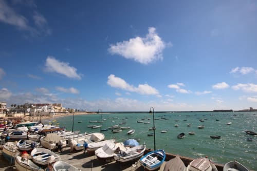 Coloridas barcas de pesca amarradas en aguas turquesas de Puerto Santa María, España, con playa y edificios costeros