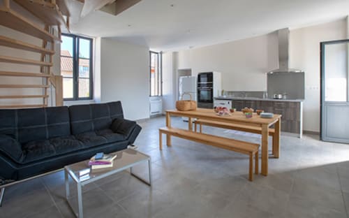 Intérieur de cottage moderne à La Maison De Siloe : séjour ouvert, canapé noir, table en bois et cuisine équipée