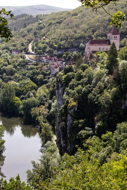 Église dominant le village de Villefranche de Rouergue niché dans une vallée boisée avec rivière