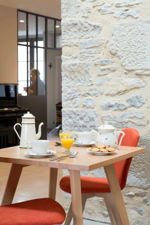 Table du petit-déjeuner à La Maison De Siloe B&B à Villefranche de Rouergue avec chaises orange, café et pâtisseries contre la pierre