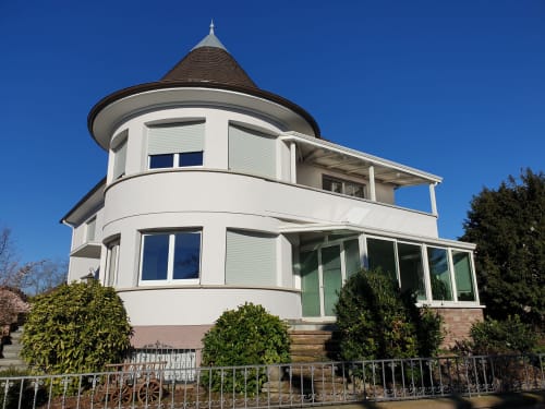 Das Cottage La Tour De L'ill in Strasbourg mit charakteristischem weißem Rundturm und Türmchen mit Blick auf den Fluss
