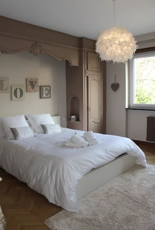 Chambre élégante à La Tour De L'ill Strasbourg avec literie blanche, luminaire plume suspendu et décoration murale taupe