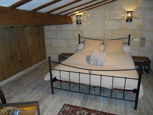Chambre rustique aux Sous Les Marronniers avec lit en fer, murs en pierre, poutres apparentes et vue sur le jardin à Petit Palais Cornemps