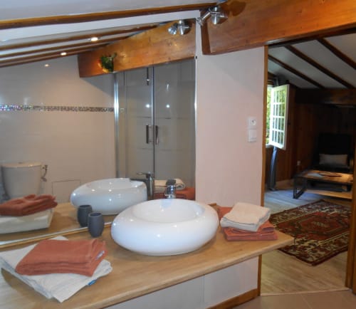 Salle de bains luxueuse aux Sous Les Marronniers avec vasques blanches doubles, poutres en bois, douche vitrée et serviettes terracotta