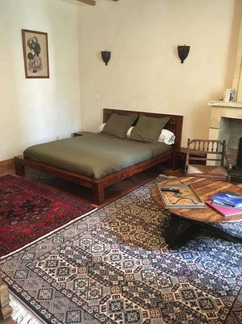 Chambre à Sous Les Marronniers avec lit en bois, linge de lit olive, tapis orientaux, cheminée et œuvres d'art murales au Petit Palais