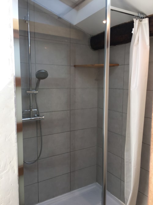 Douche à l'italienne moderne aux murs en carrelage gris, pommeau de douche manuel et étagère en bois au cottage Sous Les Marronniers