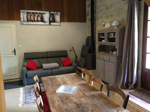 Séjour et coin repas du gîte Sous Les Marronniers avec table en bois, chaises, canapé gris et meuble de rangement à Petit