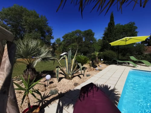Espace piscine ensoleillé au Domaine à l'Aise B&B à Saint-Pargoire avec eau bleue, parasol jaune, transats et palmiers
