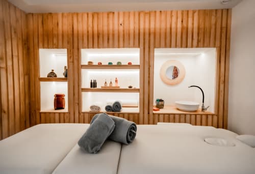 Modern spa-style bedroom at Le Pignié B&B with wooden accent wall, built-in shelving, and rolled towels on bed