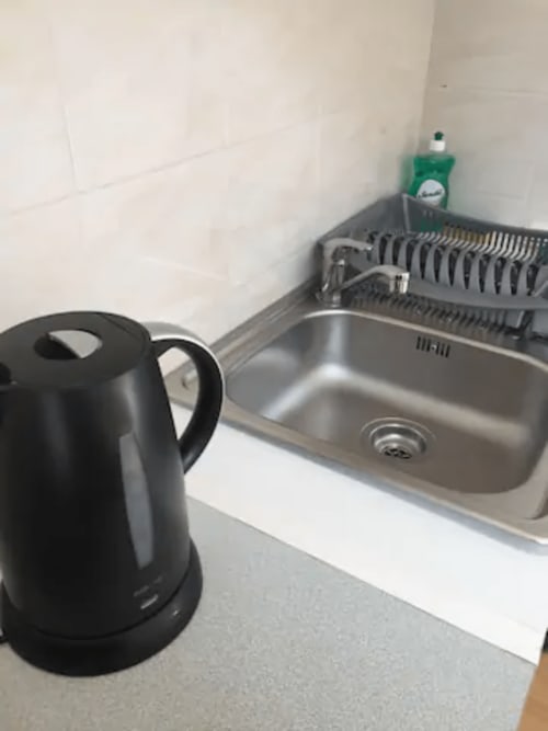 Bouilloire noire sur le plan de travail de la cuisine avec évier et égouttoir à l'appartement Résidence Mantekila à Marcinelle