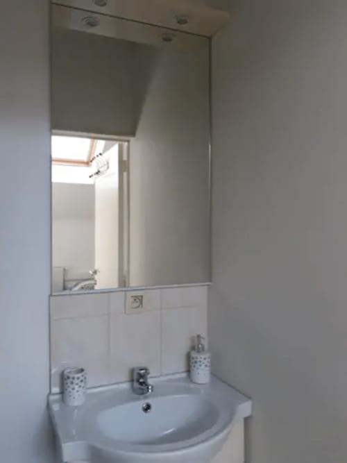 Salle de bain immaculée avec lavabo blanc, miroir et carrelage aux murs, à la résidence Mantekila à Marcinelle