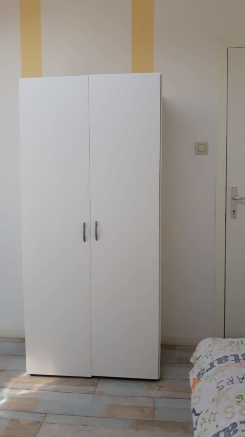 Armoire blanche dans la chambre de l'appartement de la Résidence Mantekila à Marcinelle, avec parquet et murs à rayures beiges