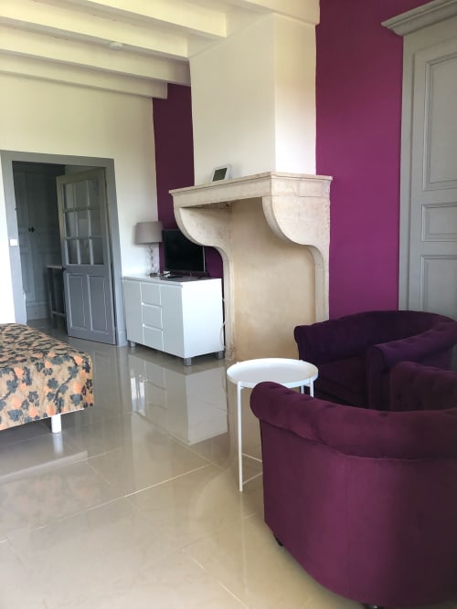 Coin salon moderne à La Ferme du Bonheur avec fauteuils bordeaux, cheminée crème et mur d'accent prune