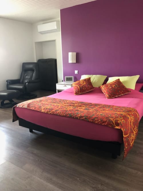 Chambre spacieuse à La Ferme du Bonheur avec mur d'accent rose, lit aux coussins colorés, fauteuil cuir noir, style moderne
