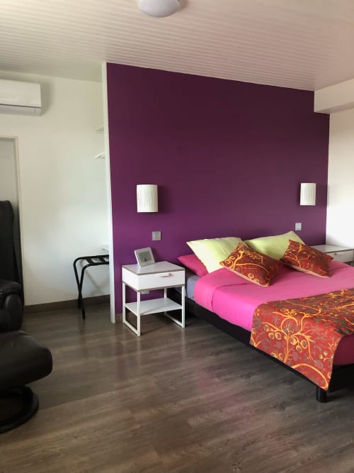 Chambre lumineuse à La Ferme du Bonheur avec mur d'accent violet, lit rose, coussins décorés et équipements modernes à Arbigny