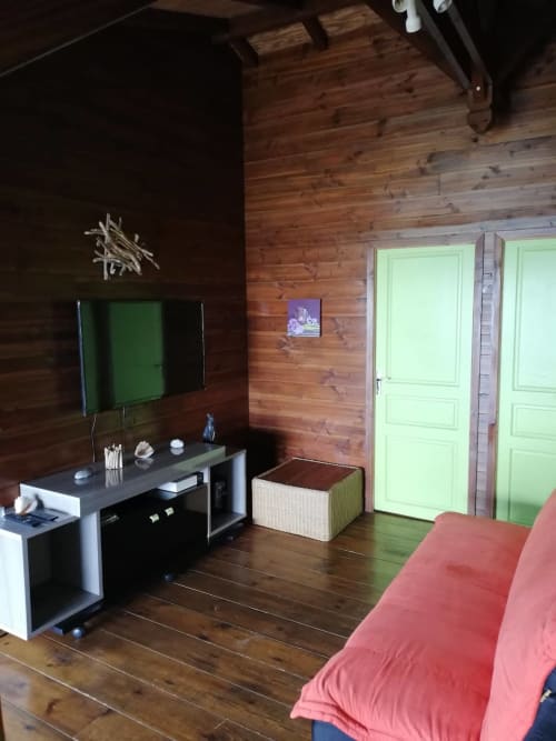 Chambre de villa moderne aux Hauts De Deshaies avec murs en bois, téléviseur, portes vertes et literie corail à Deshaies