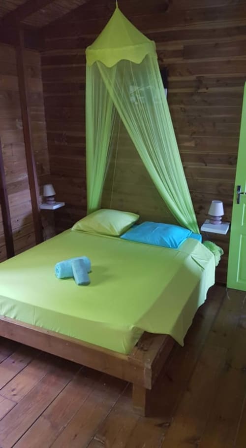Chambre de villa vert citron éclatant avec lit à baldaquin, oreillers bleus, poutres en bois et décor côtier de Deshaies