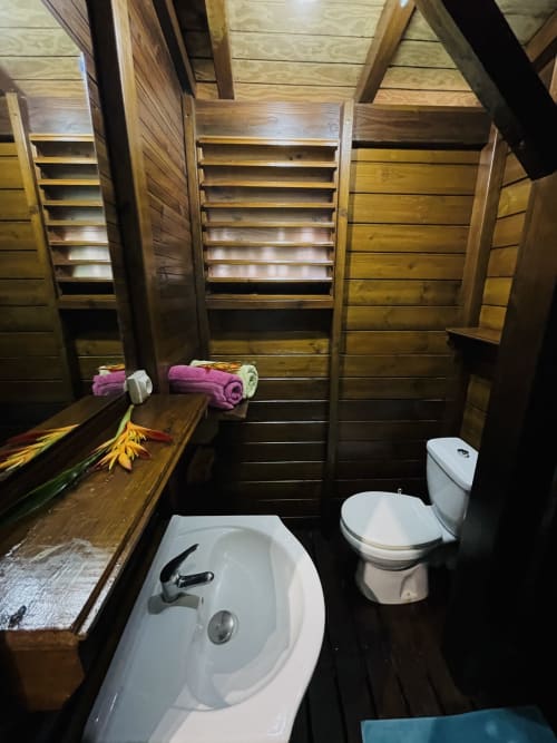 Salle de bains rustique aux murs en bois, lavabo et toilettes blancs à la villa Les Hauts De Deshaies à Deshaies