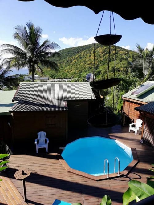 Piscine du resort Les Hauts De Deshaies avec vue sur les montagnes, terrasse en bois et cadre tropical en Guadeloupe