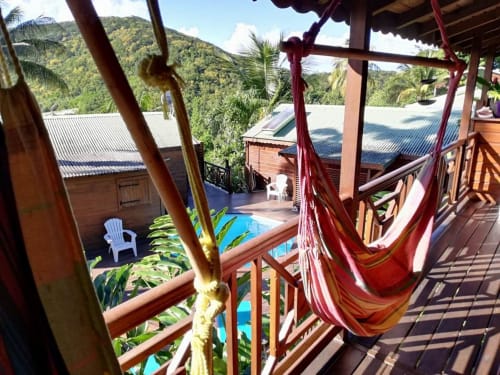 Hamac rouge sur une terrasse en bois dominant la piscine et les montagnes luxuriantes des Hauts de Deshaies, Guadeloupe