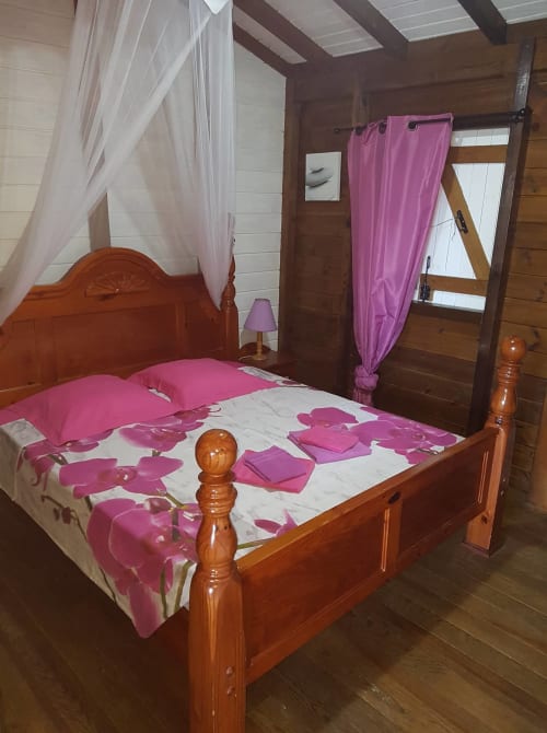 Lit à quatre colonnes en bois avec literie rose à motifs floraux dans un appartement rustique aux Hauts de Deshaies