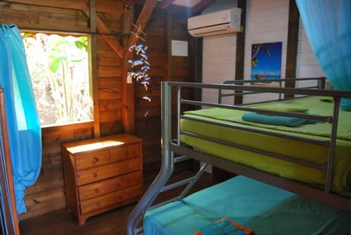 Chambre lumineuse du dortoir Les Hauts De Deshaies avec lits superposés métalliques, literie verte, bureau en bois et rideaux turquoise