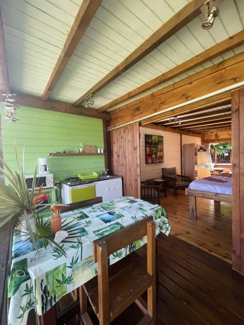 Lumineux appartement tropical aux Hauts de Deshaies : murs verts, poutres en bois, kitchenette, table à manger et chambre